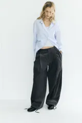 Camisa oversize de algodón con estampado de rayas finas, cuello solapa, escote en pico y manga larga con puños abotonados. Presenta un diseño con pliegues laterales y cierre frontal con botones.