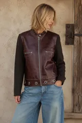 Campera de cuero marrón con mangas de lana en color marrón oscuro. Presenta cierre frontal, bolsillos con cierre en el pecho y detalle de ojales metálicos en el ruedo.