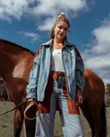 Campera de denim de corte oversize con paneles de cuero en tono habano en los hombros y mangas. Presenta cierre frontal, cuello camisero y bordado distintivo en el pecho.