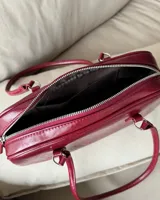 Cartera tipo baguette de cuero sintético color borgoña, con doble asa corta y cierre superior con cremallera.