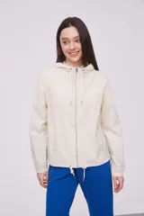 Campera liviana color crema con capucha, cierre frontal completo y cordones ajustables en el cuello y el ruedo. Cuenta con mangas largas con puños elásticos y bolsillos laterales.