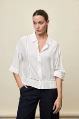 Camisa blanca de calce relajado, con cuello clásico, mangas 3/4 y cierre frontal con botones. Presenta detalles calados en el frente y en las mangas.