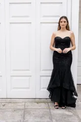 Vestido largo negro strapless tipo corset con tul y lentejuelas, de corte sirena y falda con volados.