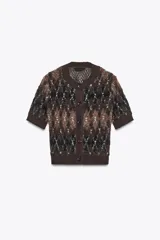 Chaqueta de punto texturizado con cuello redondo y manga corta. Presenta un patrón de rombos en tonos marrón oscuro, negro y blanco. Cierre frontal con botones oscuros.