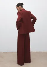 Pantalón de tiro medio color bordó, de diseño wide leg con pinzas delanteras y bolsillos laterales. Cuenta con cierre de cremallera, botón y ganchos ocultos con tapeta, además de forro interior.