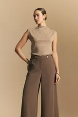 Pantalón ancho color tostado, de silueta fluida y cintura elastizada. Presenta una pretina ancha con botones metalizados irregulares.