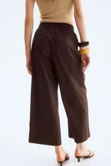 Pantalón de algodón color marrón oscuro, tiro alto, con cintura elástica y corte ancho tipo culotte o pierna ancha que termina a la altura del tobillo.