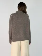 Sweater de punto gris con cuello alto y detalles de líneas negras contrastantes en los hombros y mangas. Presenta puños y ruedo acanalados.