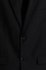 Blazer negro de corte slim fit, con solapas de muesca finas, ojal decorativo, botonadura sencilla, bolsillo superior insertado, bolsillos delanteros con solapa, dos bolsillos interiores, botones decorativos en los puños y abertura doble atrás.