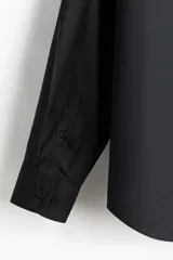 Camisa H&M de manga larga, color negro, con cuello inglés, cierre frontal de botones y corte regular fit.