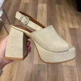 Sandalia de plataforma y taco alto, color beige claro con textura de piel de reptil. Presenta una capellada ancha que cubre los dedos y el empeine, y una tira ajustable con hebilla metálica en el tobillo.