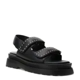 Sandalias negras estilo chunky de plataforma con suela dentada y dos tiras anchas con cierre de velcro, decoradas con tachas metálicas doradas.