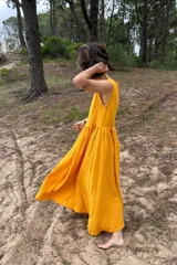 Vestido largo color amarillo de muselina de algodón, sin mangas, con corte fruncido en la cintura y falda amplia con movimiento.