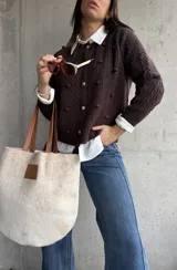Cardigan de punto color chocolate, con diseño de trenzas y pompones decorativos. Presenta cuello redondo, cierre frontal con botones metálicos dorados y mangas largas.