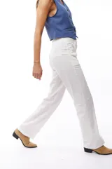 Pantalón blanco de corte recto, con bolsillos laterales y traseros. Se ajusta a la cintura con cinturón de cuero marrón.