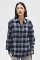 Camisa de algodón con estampado de cuadros en tonos azules, blancos y marrones. Presenta cuello camisero, cierre frontal con botones y mangas largas con puños abotonados. Su diseño es de corte holgado.
