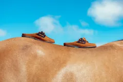 Mules de cuero color habano con detalles en azul marino, diseño inspirado en el mocasín clásico sin talón, con cordones decorativos y suela plana.