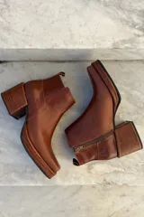 Bota corta de cuero color marrón, con taco cuadrado texturizado y punta cuadrada. Presenta un diseño minimalista con cierre lateral y tirador en la parte trasera.