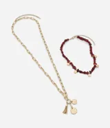 Collar doble en capas con baño en tono dorado. Una de las piezas presenta piedras irregulares en color bordó con pequeñas medallas circulares, mientras que la otra consiste en una cadena de eslabones alargados con un dije de borla y medallas texturizadas.