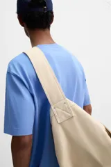 Bolso de hombro de diseño minimalista confeccionado en tejido de algodón. Cuenta con un compartimento principal con cierre de solapa con doble imán y botón a presión, además de bolsillos interiores. Incluye asa de hombro fija.