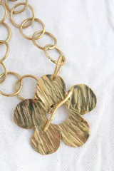 Collar de cadena dorada con eslabones circulares y dije de flor con textura.