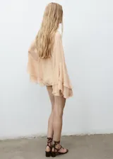 Blusa de viscosa color beige, con diseño de volantes frontales, cuello escotado con cierre de lazo y mangas largas acampanadas con volantes en los puños.