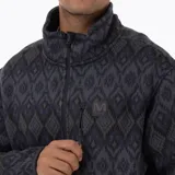 Campera polar con cierre frontal completo, confeccionada en tejido exterior tipo punto con estampado geométrico en tonos oscuros. Cuenta con cuello alto, bolsillos laterales y un bolsillo vertical en el pecho con cierre, además de un parche con el logo de la marca.