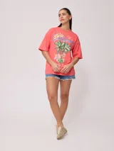 Remera color amarillo pastel con estampado de palmeras, flores de hibisco y texto 'California Ride the Tide Rusty Tribe'.