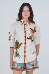Camisa de algodón color blanco, de corte clásico con cuello camisero, manga larga y cierre frontal abotonado. Presenta un estampado tropical con palmeras y tigres, y detalles de ribetes a rayas en el cuello, la botonadura y los puños.