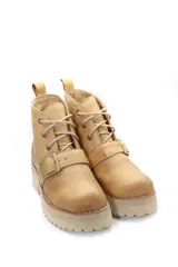 Borcego de cuero color beige con cordones, suela track de goma y detalle de hebilla metálica en el empeine.