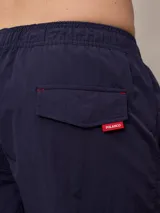 Short de baño azul marino con cintura elástica ajustable con cordón y logo de la marca bordado en rojo en la pierna izquierda.