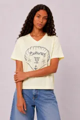 Remera de manga corta y cuello en V color amarillo claro, con estampado frontal que incluye un diseño de concha marina, estrellas de mar, un ancla y la inscripción "Bahamas Holidays on the Beach".