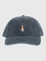 Gorra de estilo clásico con efecto lavado, confeccionada en algodón orgánico. Presenta un bordado central de un perro Basset Hound y cuenta con ajuste mediante hebilla metálica en la parte posterior.