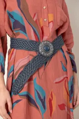 Cinto ancho de cuero trenzado color gris oscuro, con hebilla metálica redonda y ornamentada, con un cabujón central de piedra azul oscuro.