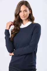 Buzo tejido en hilo de algodón color beige, con cuello redondo y manga larga. Presenta un corte clásico y un pequeño detalle metálico en la parte inferior izquierda.