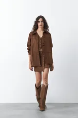 Minifalda de gamuza símil color marrón, con diseño envolvente tipo wrap, detalle de tachas metálicas en el frente y cinturón integrado con aro metálico.