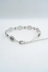 Cinturón blanco de estilo western con apliques metálicos plateados grabados y tachas decorativas. Cuenta con hebilla metálica a juego y diseño de eslabones ovalados.