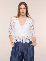 Bolero corto de encaje blanco con motivo floral y transparencias, escote en V pronunciado y mangas tres cuartos.