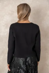 Cardigan de punto fino color negro con escote en V, manga larga y cierre frontal con botones dorados labrados, destacando un botón joya superior en forma de flor.