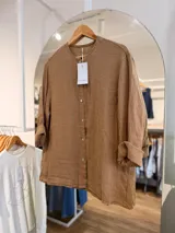 Camisa de lino color marrón, de silueta relajada y corte oversize, con cuello mao, mangas largas remangadas y cierre frontal con botones.