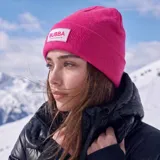 Gorro tipo beanie de tejido de punto en color fucsia, con vuelta en el borde y parche rectangular con el logo de la marca en la parte frontal.