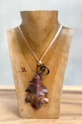 Collar con dije de hoja de roble color cobre, con cadena de cuero color beige.