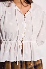 Blusa negra de algodón con diseño de broderie, mangas tres cuartos abullonadas, cierre frontal con botones y detalle de cordón ajustable en la cintura.