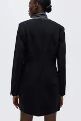 Vestido corto negro de sarga con escote redondo, hombreras finas y mangas largas con abertura en los puños. Presenta cintura entallada con pinzas, bolsillos ribeteados con solapa en el frente y cierre oculto en la parte trasera. Forrado.