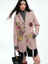 Blazer de corte recto con estampado de cuadros en tonos rosados, presenta bordados florales coloridos en el frente y un parche estilo escudo en el bolsillo superior. Cuenta con cierre frontal de botones y detalles en contraste en las mangas.