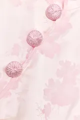 Top satinado jacquard color rosado, con cuello mao, manga muy corta y cierre lateral con cremallera oculta. Presenta detalle de botones decorativos tipo nudo chino en el delantero y diseño con estampado floral sutil.