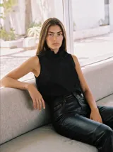 Blusa sin mangas de lino color negro, con cuello alto plisado, cierre lateral asimétrico con botones forrados y detalles de pliegues frontales.