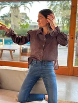 Camisa marrón de algodón con cuello clásico, cierre frontal con botones dorados y mangas largas abullonadas con puños elásticos.