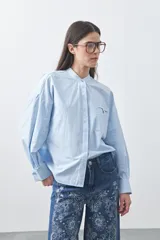 Camisa de manga larga en color celeste, con cuello mao y cierre frontal oculto. Presenta un diseño de silueta relajada con sisa caída y un bolsillo aplicado en el pecho.