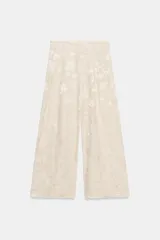 Pantalón de tiro medio confeccionado en hilatura con lino, con cintura con trabillas, bolsillos laterales ocultos y pierna ancha. Presenta un diseño con estampado jacquard de motivos florales en tonos beige y crudo, y cierre frontal con cremallera, botón y ganchos metálicos.